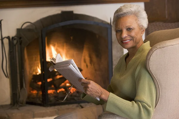 新聞を笑顔で暖炉のそばでリビング ルームに座っている女性 — ストック写真
