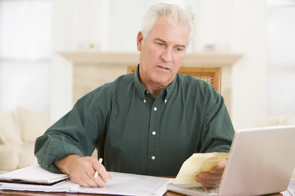 Man in dining room with laptop and paperwork looking unhappy — Stock Photo, Image