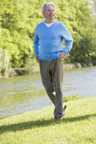 Человек гуляет по парку у озера улыбаясь — стоковое фото