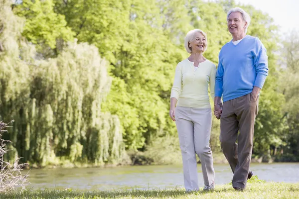 Couple walking outdoors at park by lake smiling — Stock Photo, Image