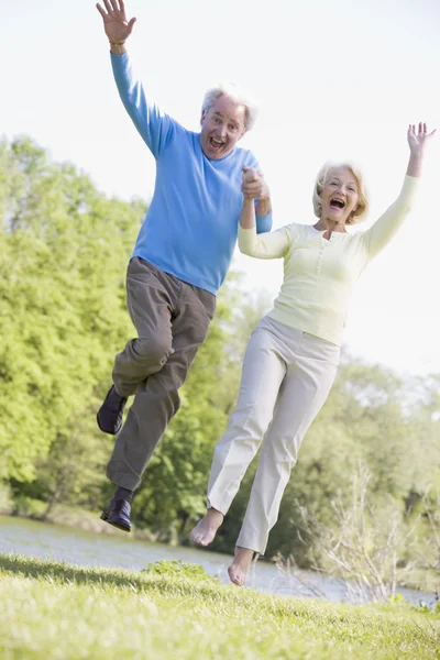 Paar springt lächelnd im Park am See — Stockfoto