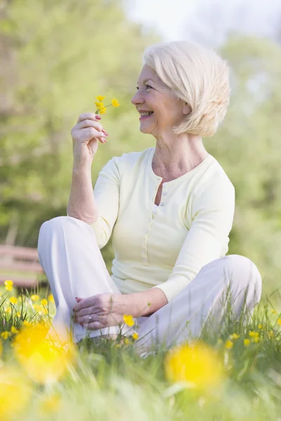 Woman sitting outdoors smiling and holding a Buttercup flower — Stock Photo, Image