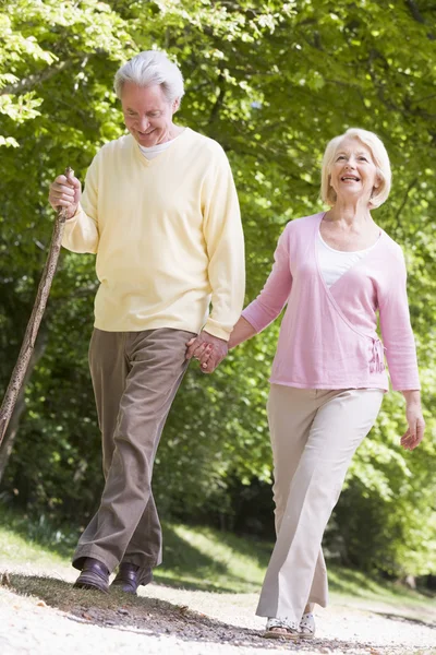 Пара прогулок по дорожке в парке, держась за руки и улыбаясь — стоковое фото