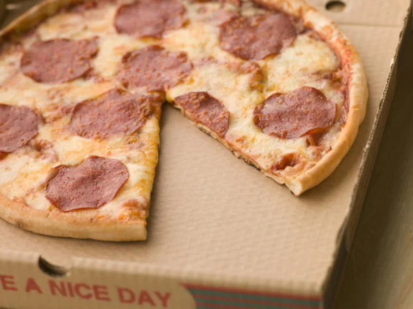Pizza al salame piccante in una scatola da asporto con una fetta presa — Foto Stock
