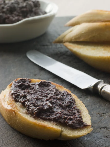Черная оливковая тапенада с поджаренным багетом — стоковое фото