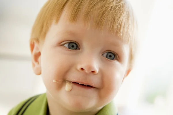 Young boy eating baby food with mess on face — Stockfoto