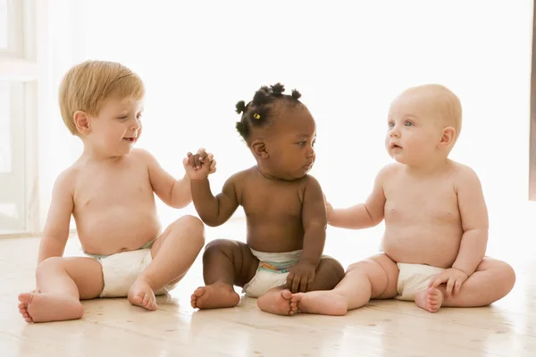 Três bebês sentados dentro de casa de mãos dadas — Fotografia de Stock