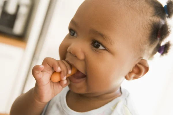 Jong meisje eten wortel binnenshuis — Stockfoto