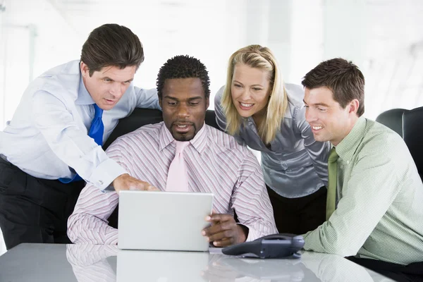 Cuatro empresarios en una sala de juntas apuntando a la computadora portátil y sonriendo —  Fotos de Stock