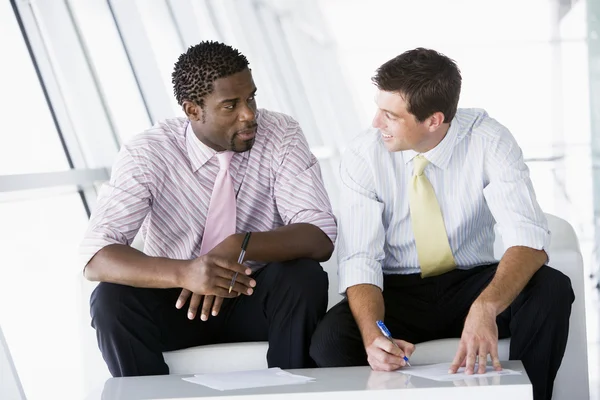 Two businessmen sitting in office lobby talking and smiling — Stock Photo, Image