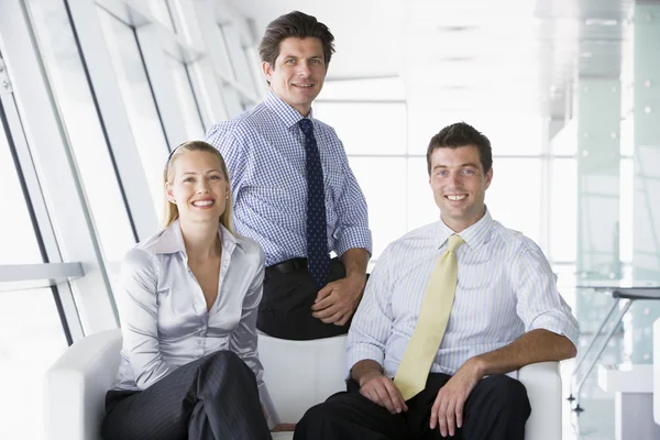 Трое бизнесменов сидят в офисном холле и улыбаются — стоковое фото