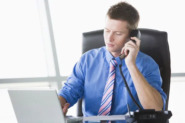 Businessman sitting in office with laptop on telephone — Stock Photo, Image