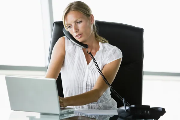 Geschäftsfrau sitzt mit Laptop am Telefon im Büro — Stockfoto