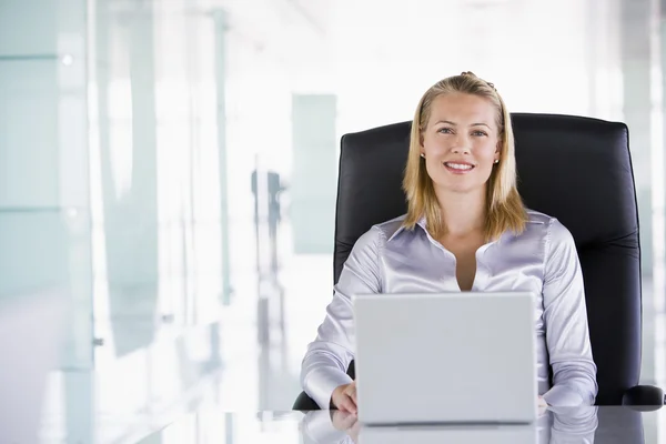 Businesswoman sitting in office with laptop smiling — Stock Photo, Image
