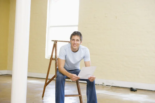 Чоловік сидить на драбині в порожньому просторі тримає папір посміхаючись — стокове фото