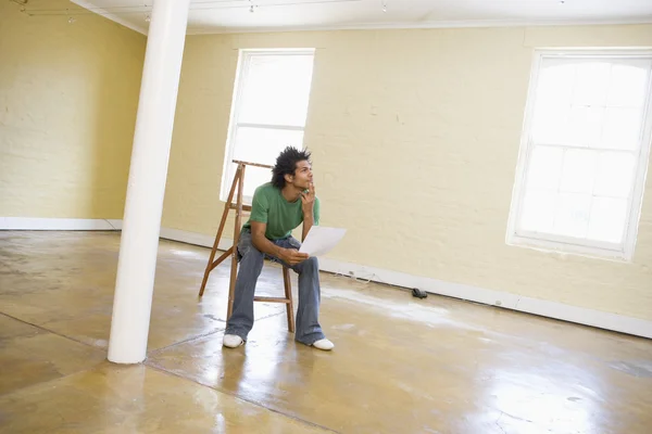 Homme assis sur l'échelle dans un espace vide tenant le papier pensant — Photo