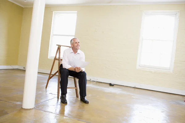Mann sitzt auf Leiter im leeren Raum und hält lächelndes Papier — Stockfoto