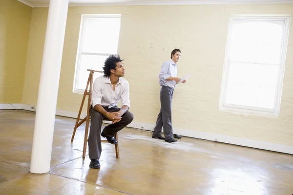 Man sitting on ladder in empty space with another man holding pa — Stock Photo, Image