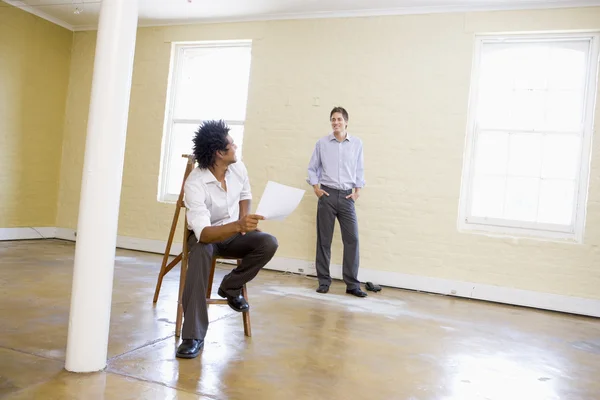 Man sitting on ladder in empty space holding paper talking to ot — Stock Photo, Image