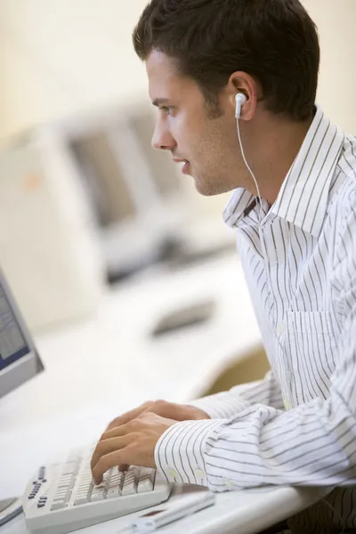 Hombre en la sala de computadoras escuchando el reproductor de MP3 mientras escribe — Foto de Stock