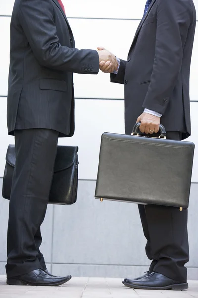 Due uomini d'affari che tengono le valigette all'aperto stringendosi la mano — Foto Stock