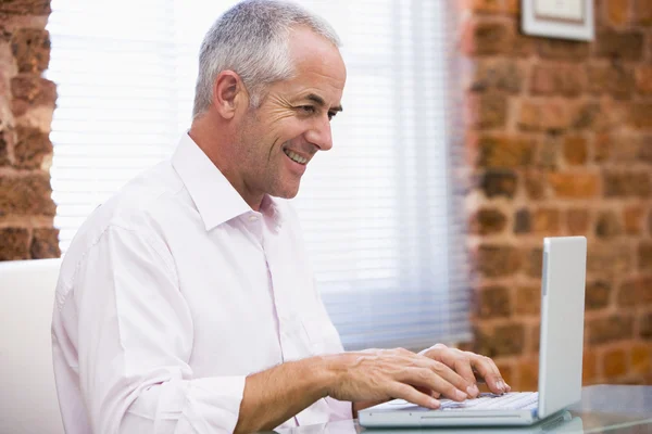 Бизнесмен сидит в офисе и печатает на ноутбуке улыбаясь — стоковое фото