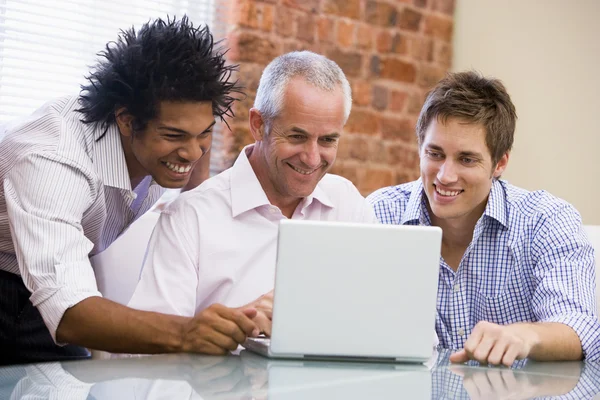 三个商人坐在办公室用笔记本电脑微笑 — 图库照片