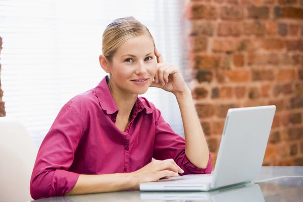 Kobieta siedzi w biurze z laptopa uśmiechający się — Zdjęcie stockowe