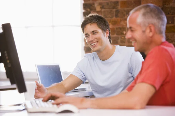 Два бизнесмена в офисе печатают на компьютере и улыбаются — стоковое фото