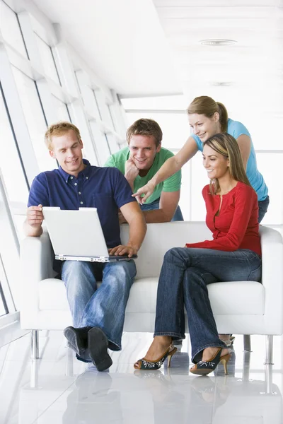 四个在大厅指着笔记本电脑微笑 — 图库照片