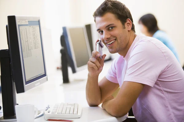 Hombre sentado en la sala de computadoras usando el teléfono celular y sonriendo —  Fotos de Stock