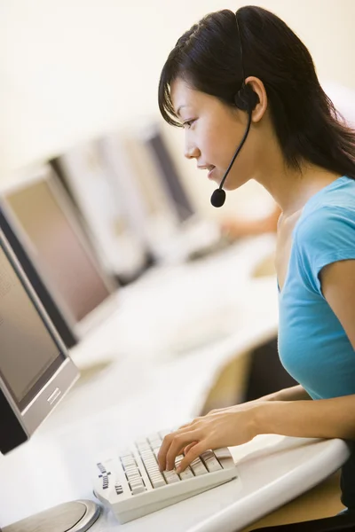 Mulher vestindo fone de ouvido sentado na sala de informática digitação — Fotografia de Stock
