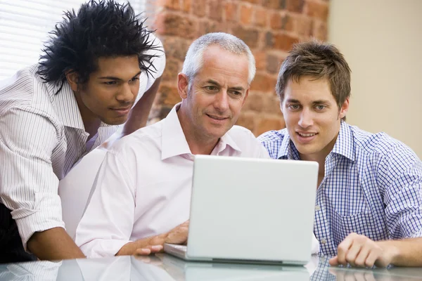 Trzech biznesmenów w biurze patrząc na laptopie uśmiechający się — Zdjęcie stockowe