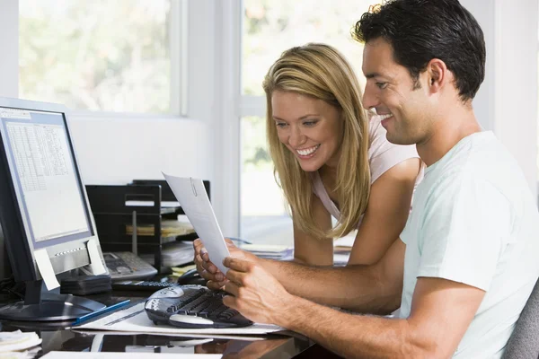 Пара в домашнем офисе с компьютером и бумажной работой улыбается — стоковое фото