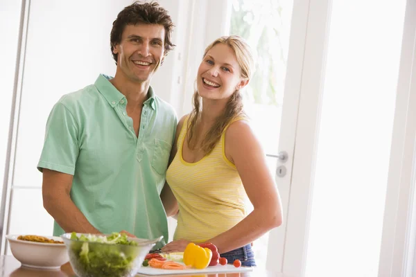 Par i köket skär upp grönsaker och ler — Stockfoto