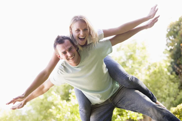 Man geven vrouw piggyback rit buiten glimlachen — Stockfoto