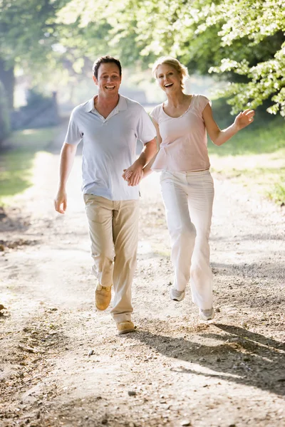 Casal correndo ao ar livre de mãos dadas e sorrindo — Fotografia de Stock