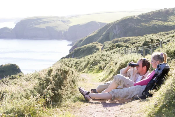 Couple on cliffside outdoors using binoculars and smiling — Stock Photo, Image