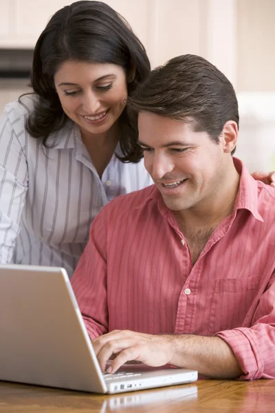Par i köket med pappersarbete med laptop leende — Stockfoto