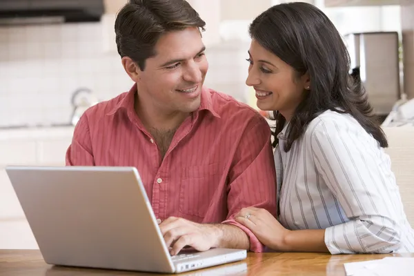Couple in kitchen using laptop and smiling — Stock Photo, Image