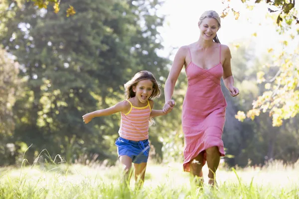 Woman and young girl running outdoors holding hands and smiling — Stock Photo, Image