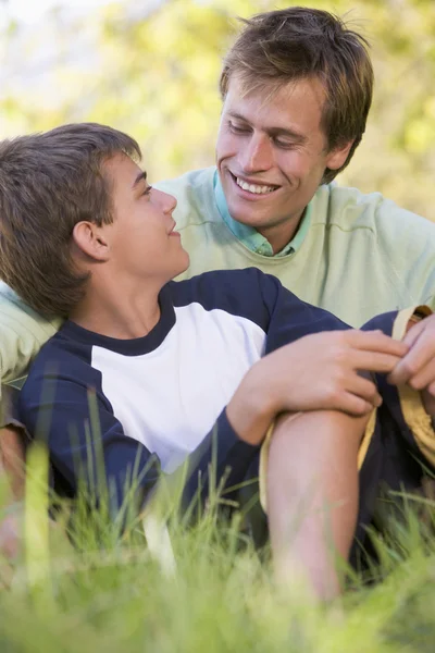 Мужчина и мальчик сидят на улице и улыбаются. — стоковое фото