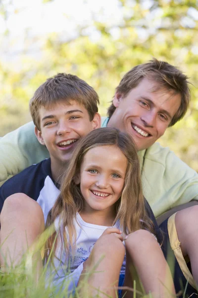 Uomo con due bambini seduti all'aperto sorridenti — Foto Stock