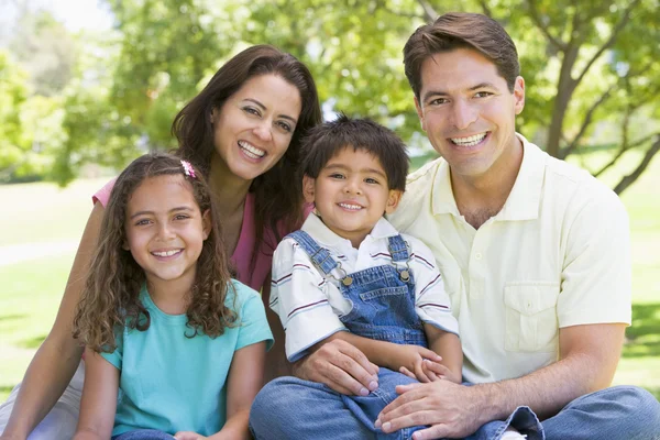 Familjen sitter utomhus leende坐在户外微笑的家庭 — Stockfoto