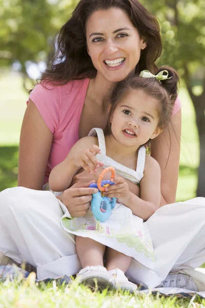 Frau und junges Mädchen sitzen draußen mit Spielzeug lächelnd — Stockfoto