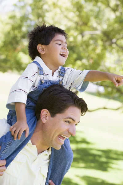 Man giving young boy shoulder ride outdoors smiling — Stock Photo, Image