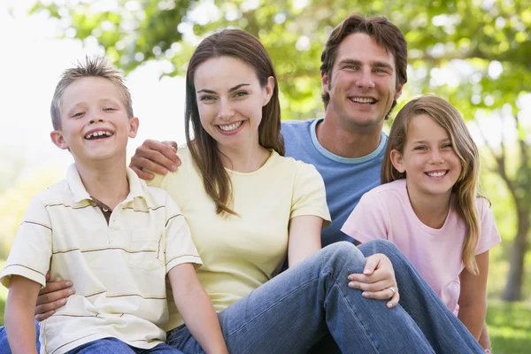 Familjen sitter utomhus leende坐在户外微笑的家庭 — Stockfoto