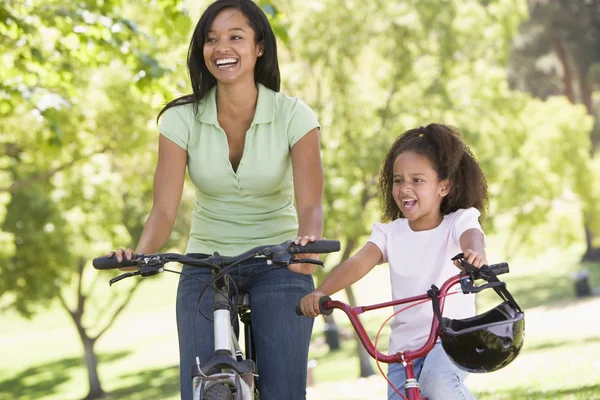 Женщина и молодая девушка на велосипедах на улице улыбаются — стоковое фото