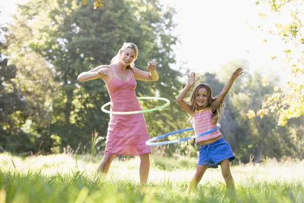 Mujer y chica joven al aire libre usando aros hula y sonriendo — Foto de Stock