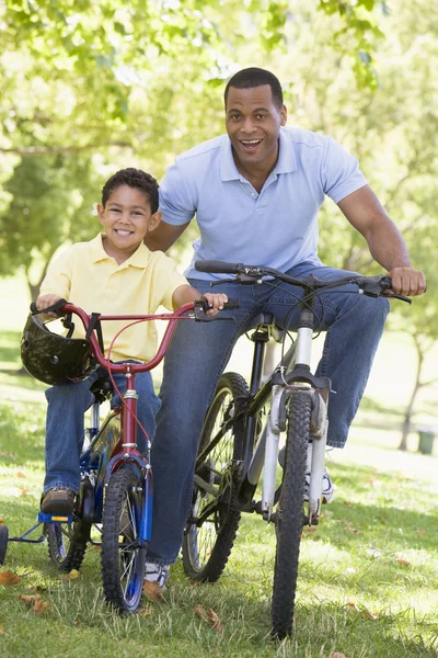 Hombre y chico joven en bicicletas al aire libre sonriendo — Foto de Stock